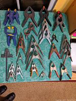 Full lot of 36 spring clamps arranged on green table, showing various sizes and styles including metal and plastic clamps