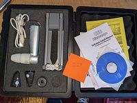 Opened carrying case showing the USB digital microscope, adjustable stand, lenses, manual, and software CD secured in custom foam.
