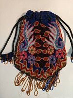 Full front view of vintage beaded purse showing colorful floral and wing designs on dark base, with bead fringes at bottom in worn condition.