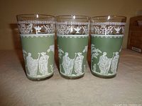 Three taller green glasses with white jasperware-style Grecian figures and detailed gold rims, front view showing different classical scenes.