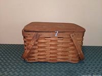 Front view with lid closed showing woven wood texture, swinging handles folded against the basket, and metal clasp at center front.