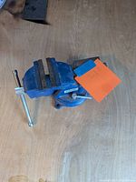 Blue metal bench vise placed on a wooden surface, showing the general condition and handle.