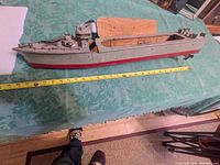 Side view of wooden toy navy boat next to measuring tape showing approx. 26-inch length