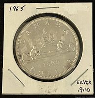 Reverse side of 1965 Canadian silver dollar coin showing canoe design and inscriptions.