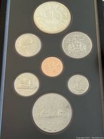 Full view of seven Canadian coins in a display case including the large silver double dollar at bottom, other smaller coins surrounding it.