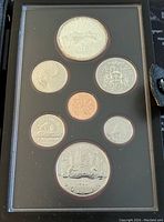 Photo showing the front of the coin display case with seven Canadian coins arranged, including two large silver dollars at top and bottom, featuring detailed engravings with Canadian themes and Queen Elizabeth II.
