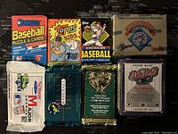 Six unopened baseball card packs from early 1990s coming from various brands with distinct packaging and logos, laid out on a dark map background.