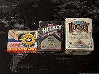 Three unopened box sets of NHL hockey cards from 1990-1992 on a black map surface.