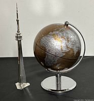 Photo showing both the 8-inch world globe on chrome stand and clear CN Tower model side by side on a black surface against a light backdrop.