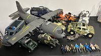 Top-down view showing the large gray military transport plane, blue SWAT van, green military jeep, and various orange/black vehicles along with military action figures spread in front.