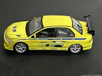 Side view of yellow Mitsubishi Lancer Evolution VII die cast model car showing racing decals and spoiler.