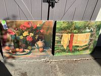 Both paintings side by side leaning against wall under natural light