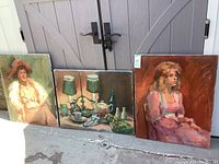 Three framed paintings on canvas by Patricia LaGrande, propped against a door. Two portraits and one still life are visible.
