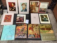 Photo of art print and 12 art books arranged in two rows on a dark surface