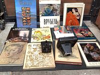 Wide view of 11 art books with 2 vintage cameras arranged on a flat surface