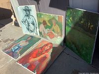 Five assorted canvas paintings arranged outdoors showing subjects including figures and landscapes.