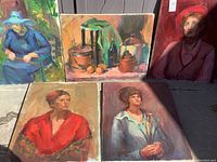 Five assorted paintings on canvas including portraits and still life arranged side by side outdoors.