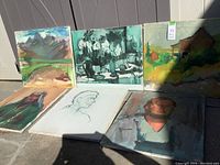 Six assorted paintings arranged on ground, including landscapes, portraits, and a still life, with varied color palettes.