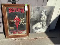 Beefeater branded advertising mirror next to grayscale figurative art painting, shown together in sunlight.