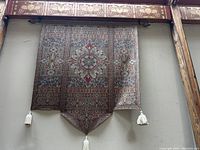 Full view of the finely made wall hanging tapestry hung on a wall. Shows overall design and tassels.