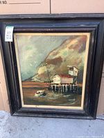 Full view of the framed painting depicting a dock, boat, and scenic background, showing the frame condition.