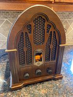 Front view of vintage style General Electric radio with wooden cathedral-style case, speaker grille, analog dial, and three knobs.