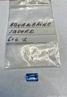 Aquamarine gemstone outside plastic bag and plastic bag with label indicating 'Aquamarine Square 6x6 2'
