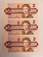 Front side of three 1986 Canadian $2 banknotes stacked, showing Queen Elizabeth II and denomination markings.