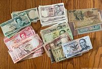Photo showing assorted banknotes from Eastern Caribbean, Indonesia, Mexico, and Colombia arranged in stacks by country and denomination on a wooden surface.