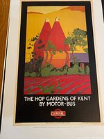 Photo of the London Underground reproduction poster titled 'The Hop Gardens of Kent by Motor-Bus' showing an illustration of red oast houses in a countryside setting with surrounding greenery and fields.