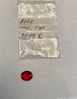 Oval shaped red ruby gemstone on white background with clear plastic bag labeled 9x11 mm size.