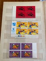 Photo showing blocks of four Hong Kong Olympics stamps, red calligraphy stamps, and hunting dog $5 stamps on purple background.