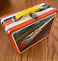 Closed vintage lunchbox showing the CN CP railroad train image on the front with vibrant colors, yellow handle, and metal latch.