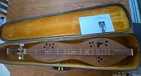 Full view of the walnut dulcimer in its yellow plush-lined hard case, shows overall shape and included instruction sheet.