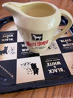 White Horse Whiskey cream ceramic pitcher on the Black & White Whiskey metal serving tray, showing front White Horse label and tray design.