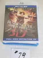 Stacked sealed Blu-ray DVDs showing Resident Evil: Afterlife 3D on top including handwritten lot number tag