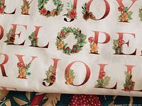 Close-up of white fabric with red and green Christmas letters and foliage