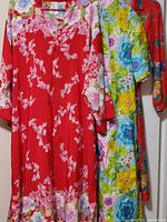 Three floral garments including a red floral piece, colorful floral robe, and red floral robe hanging on hangers