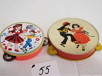 Two vintage metal tambourines, one with dancing girl and boy in colorful outfits, the other with retro dancing couple, side by side