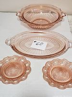 Pink Depression Glass 2-handled serving bowl, oval platter, and four small lacy edge plates arranged on a white surface