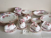Full set arranged on table showing plates, cups, and saucers with floral pattern and gold trim.