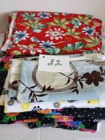 Stack of mixed fabric pieces showing red floral cotton fabric on top and multiple other colorful floral prints below with a label '32'.