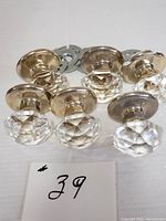 Six diamond cut glass door handles with metal bases arranged side by side on a white surface with a lot number card.