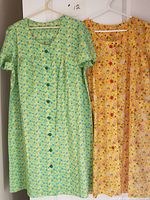 Two floral patterned dusters hanging on hangers, showing full length and front details