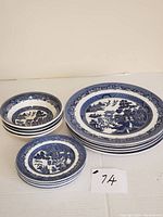 Set of 14 pieces including stacked soup/cereal bowls, dinner plates, and bread/butter plates all with blue and white Willow pattern design.
