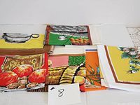 Overview of six colorful cotton kitchen towels with food and utensil themed prints laid out flat.