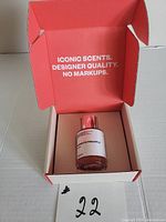 Dossier perfume bottle inside opened orange box with the text 'ICONIC SCENTS. DESIGNER QUALITY. NO MARKUPS.' on the inside lid.