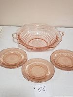 Two photos showing a set of 6 pink Depression glass plates and one pink Depression glass handled serving bowl. The bowl is placed behind the plates and shows its size and handles.