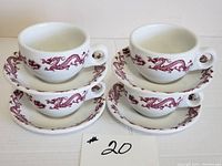 Four white cups and four matching saucers arranged in two stacks, all featuring a red dragon motif wrapping around them.