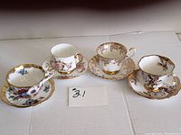 Four sets of Royal Albert bone china tea cups and saucers arranged side by side showing patterns and gold detailing.